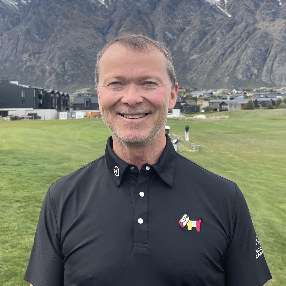 Bevan Kidd smiling on the practice ground at Jacks Point, the Remarkables snow-capped behind him