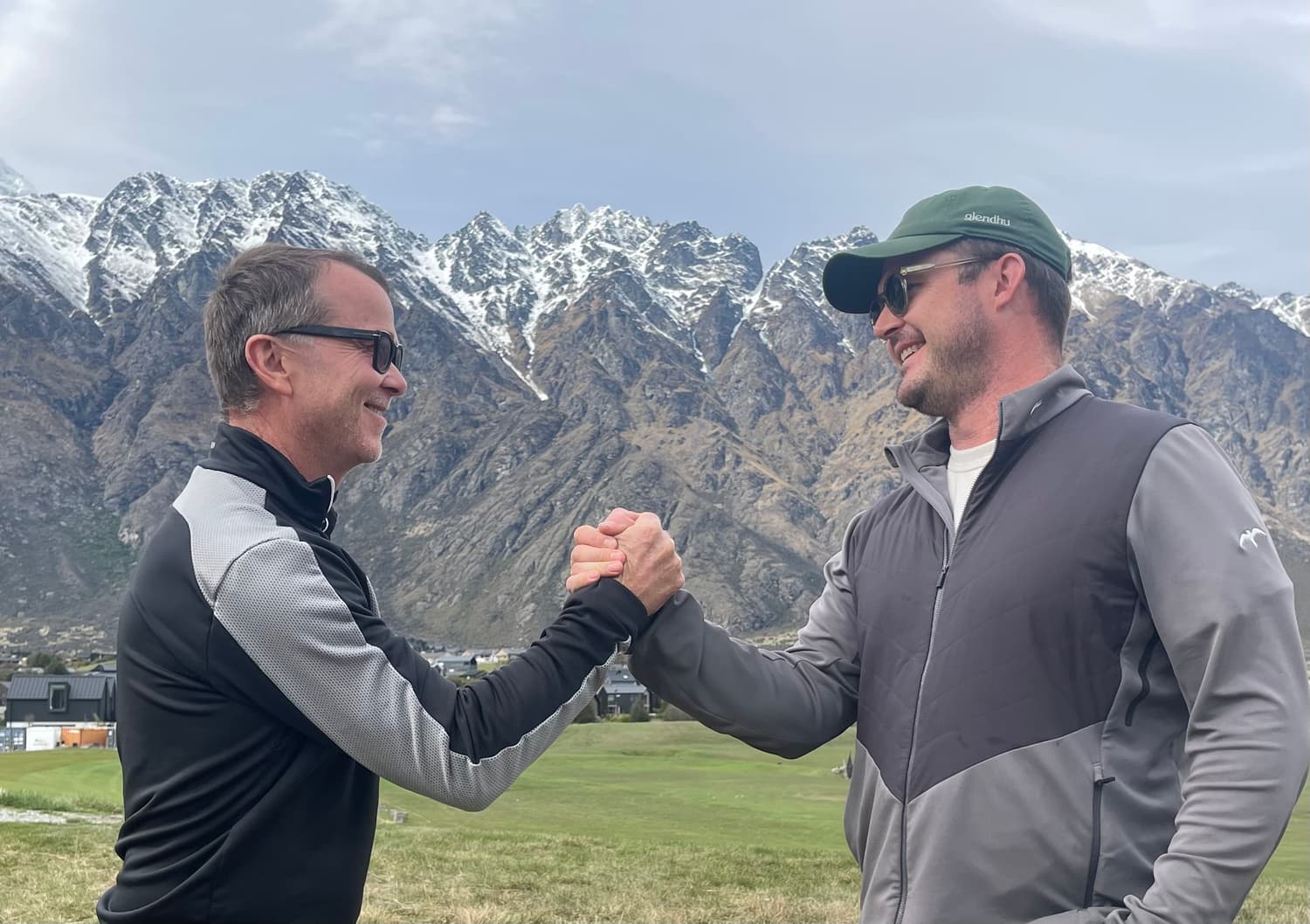 Bevan Kidd shaking hands with a student on the fairway, with snow-capped mountains behind
